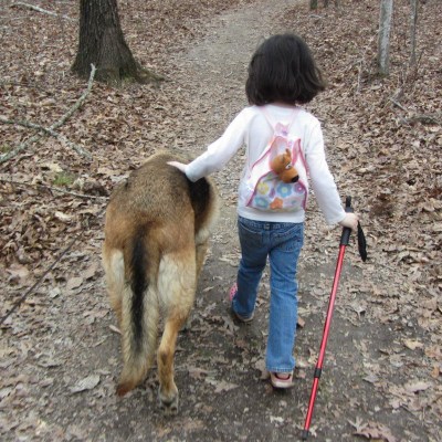 A child enjoying a hiking trail with her dog.