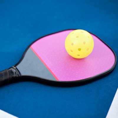 A pickleball paddle and ball on a court.