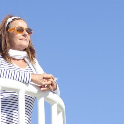 older woman with sunglasses gazes out from balcony