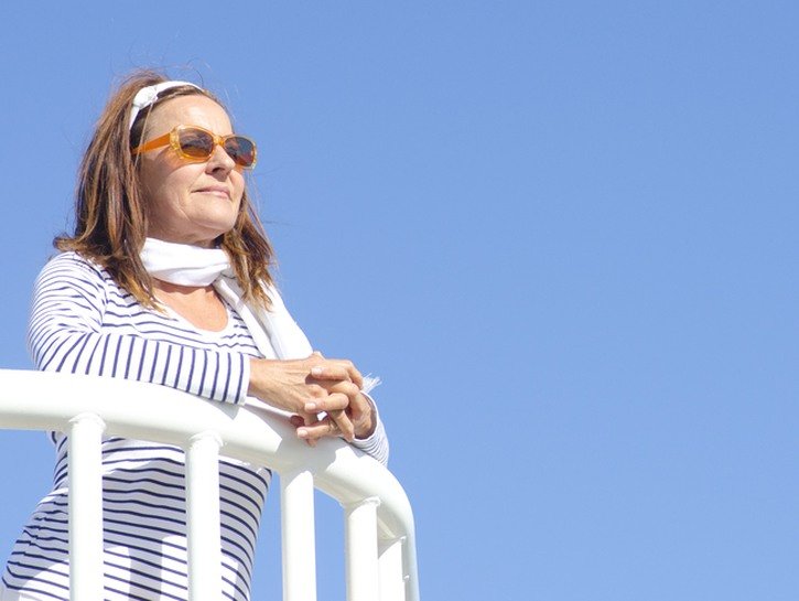 older woman with sunglasses gazes out from balcony