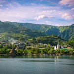 Papeete, Tahiti, shoreline with buildings and lush vegetation.