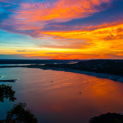 Colorful Dramatic Sunset Over Lake Travis golden and purple reflecting off water around the cove of high limestone cliffs outside of Austin , Texas Hill Country