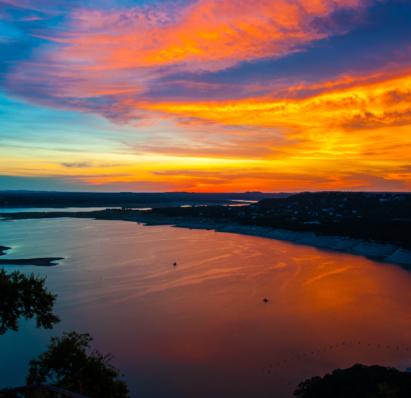 Colorful Dramatic Sunset Over Lake Travis golden and purple reflecting off water around the cove of high limestone cliffs outside of Austin , Texas Hill Country