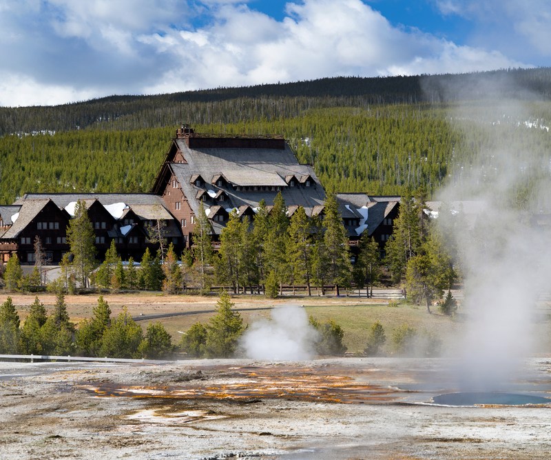 Old Faithful Inn with geysers and steam in foreground.