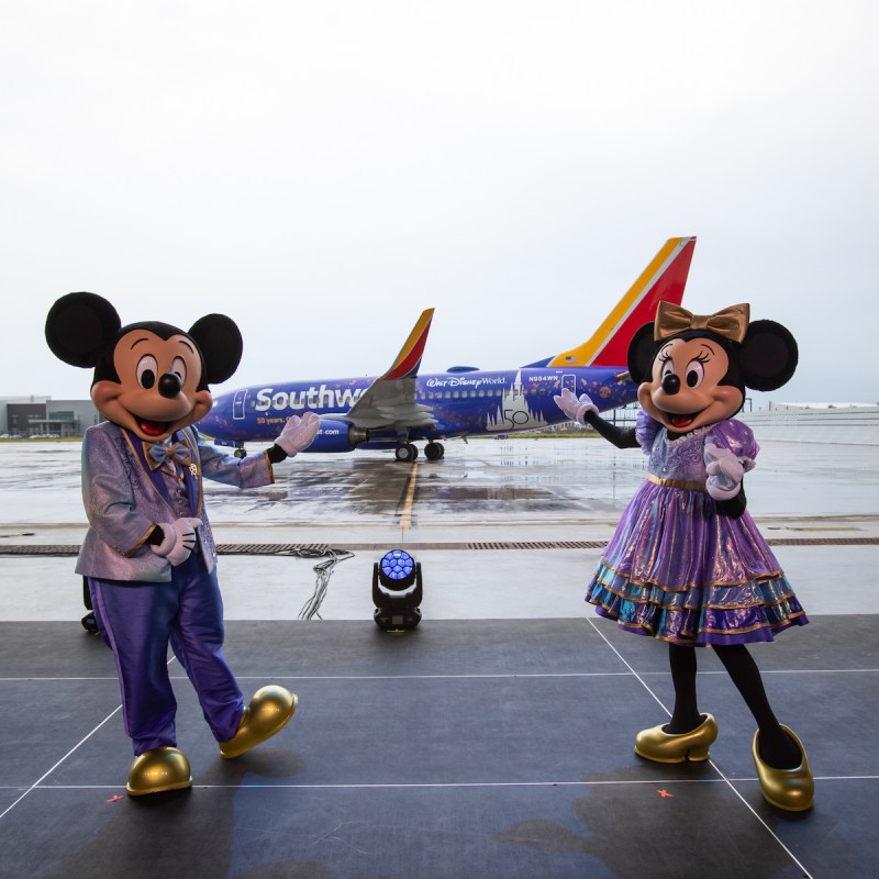 Mickey and Minnie Mouse standing in front of brand new Disney World-designed Southwest plane.
