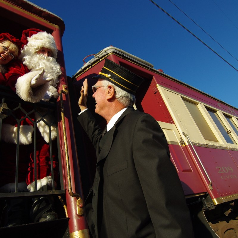 Holiday train conductor high fives santa and mrs. claus