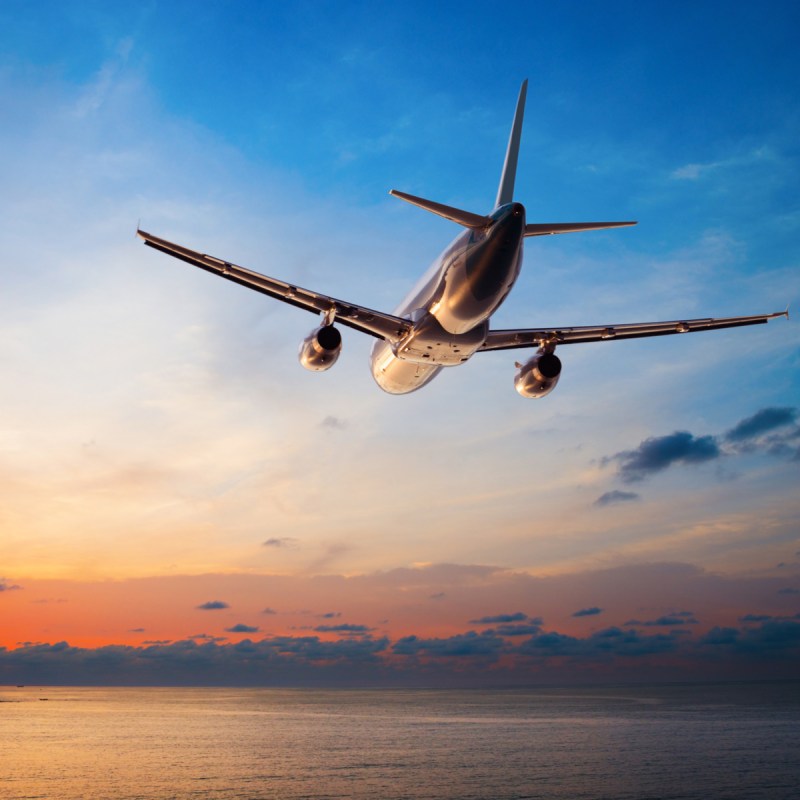 Airplane flying over body of water at sunset.