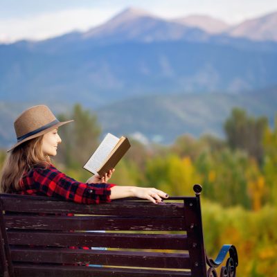 solo woman reading book in front of mountains while traveling