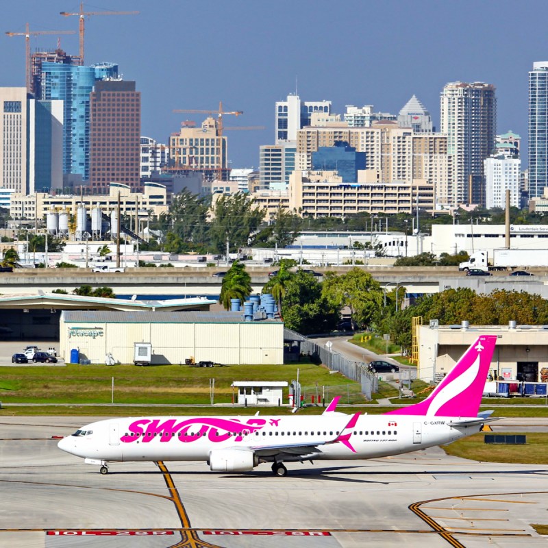 Swoop Airlines 737 about to tak off from FLL. Downtown Fort Lauderdale in background.