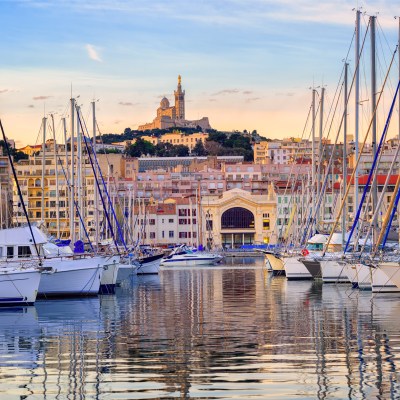 Yachts reflecting in the still water of the old Vieux Port of Marseilles beneath Cathedral of Notre Dame, France, on sunrise