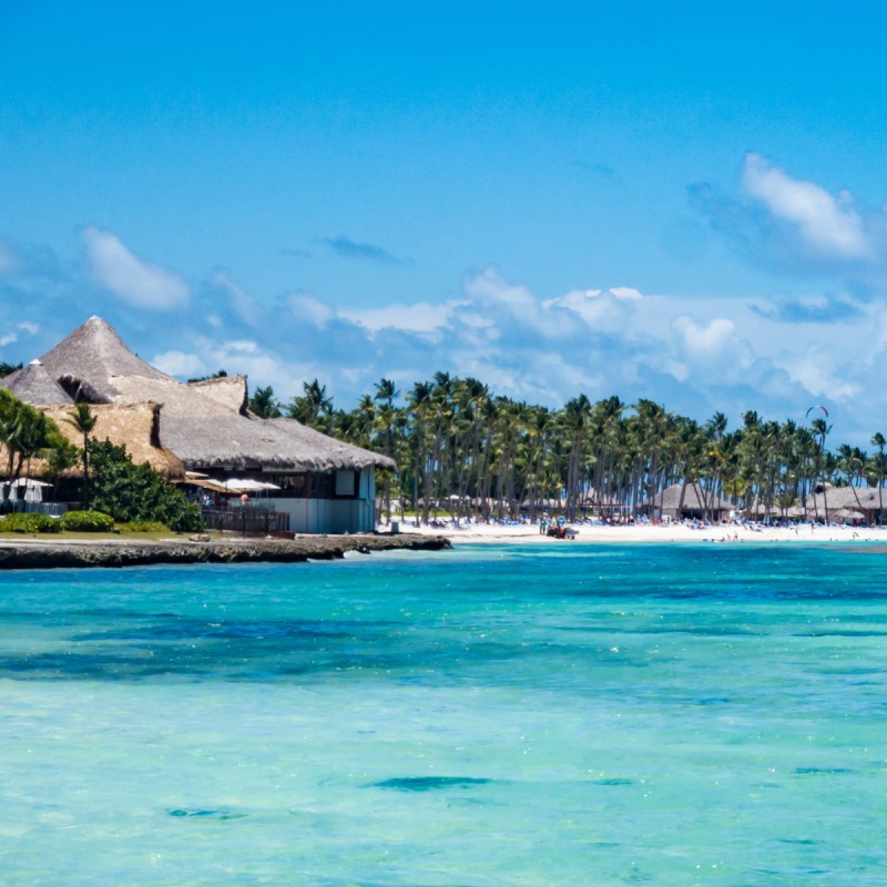 The crystal clear aqua blue Caribbean sea along the beach in Punta Cana, Dominican Republic with palm trees on a partly cloudy summer day in tropical paradise.