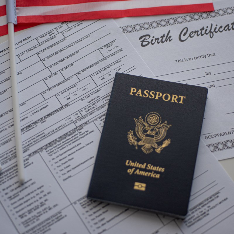 U.S. standard certificate of live birth application form next to flags of USA, passport of USA and Birth certificate blank.