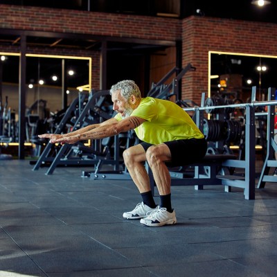 Full length of a mature caucasian man in sportswear working out at gym, doing squats.