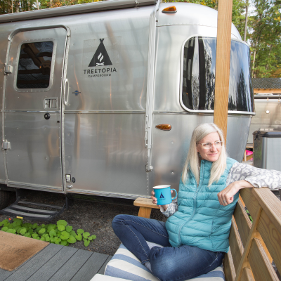 TravelAwaits writer Sage Scott drinking coffee outside of her Treetopia Airstream camper