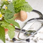 Fresh herbs, pills, and a stethoscope on a table.
