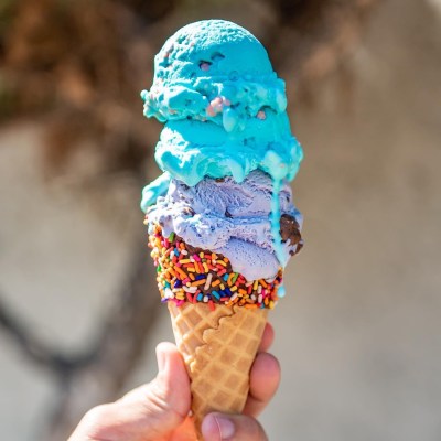 hand holding chocolate and sprinkle dipped cone with a scoop of purple and a scoop of blue ice cream from Cali Cream Homemade Ice Cream