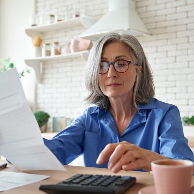 mature woman holding paper at kitchen counter doing calculations