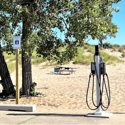 Electric vehicle charging station in Michigan's Holland State Park. Sand and a picnic table in the background.