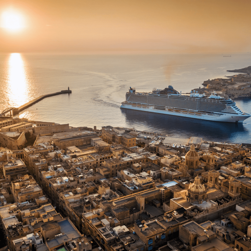 Cruise ship entering the Grand Harbour in Valletta, Malta, with the sun low over the Mediterranean.