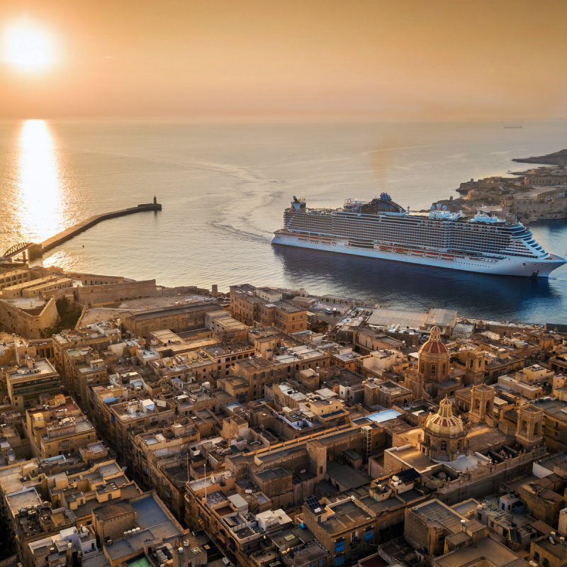 Cruise ship entering the Grand Harbour in Valletta, Malta, with the sun low over the Mediterranean.