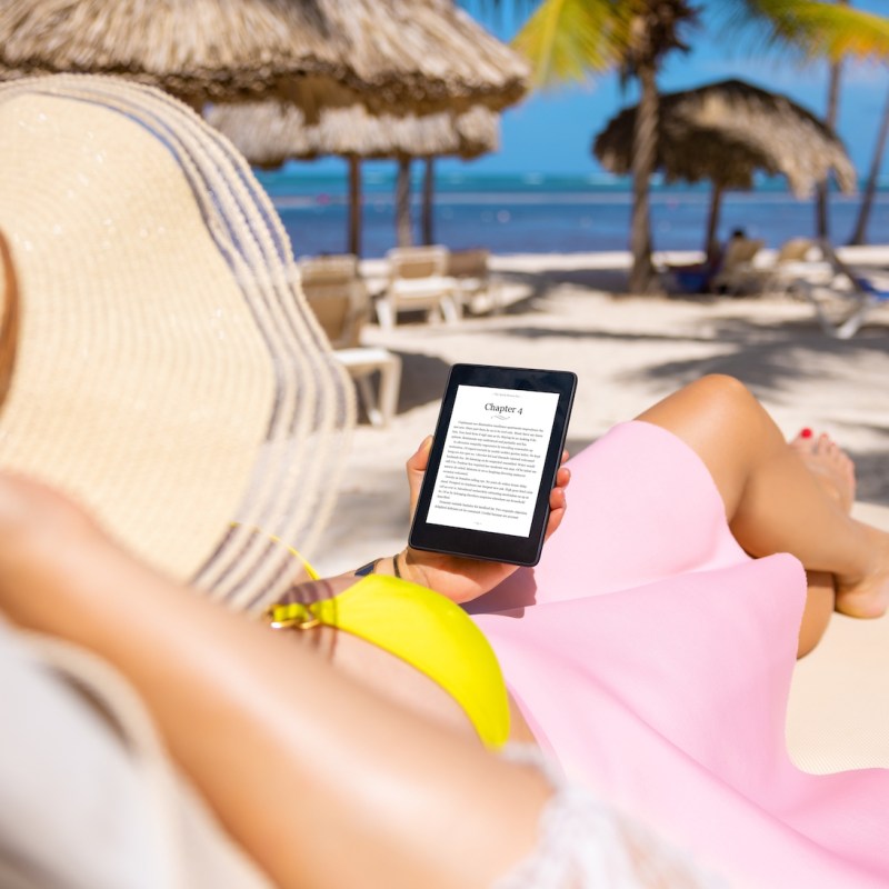 Woman holding e-reader device and reading e-book on the beach