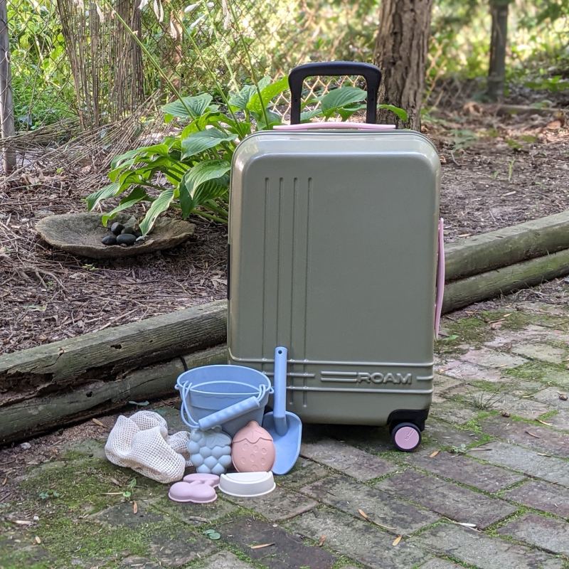 ROAM Carry-On Luggage sitting with kids toys in front of garden