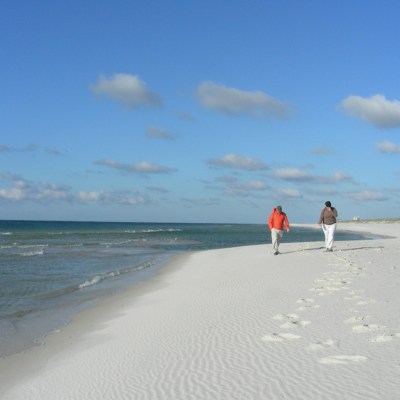A couple enjoys a walk along the Gulf on the Pine Beach Trail.