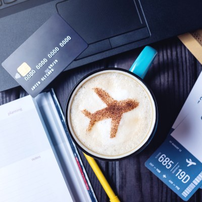 A travel credit card next to a cup of coffee with airplane latte art.