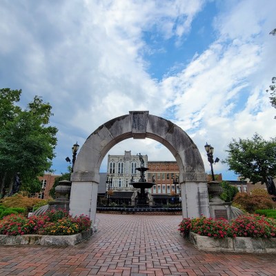 Stone archway, flowerbed, and brick walkway at the entrance to Fountain Square Park in Bowling Green