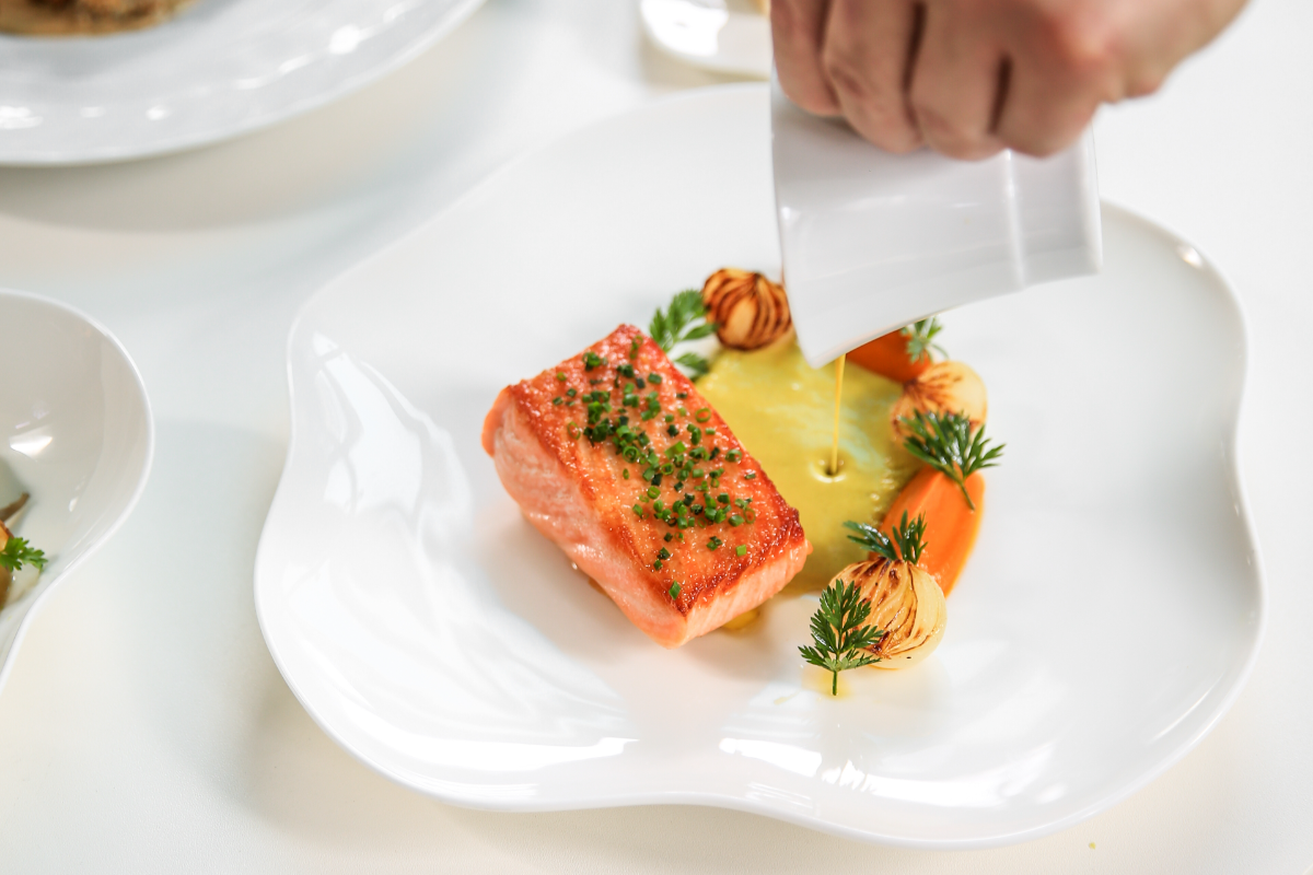 person pouring sauce on salmon dish