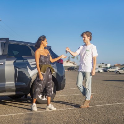 A woman traveler receiving her Kyte SUV rental keys from a Kyte “Surfer”