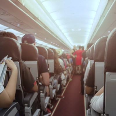 Interior of plane with flight attendants and passengers gathered down the aisle.