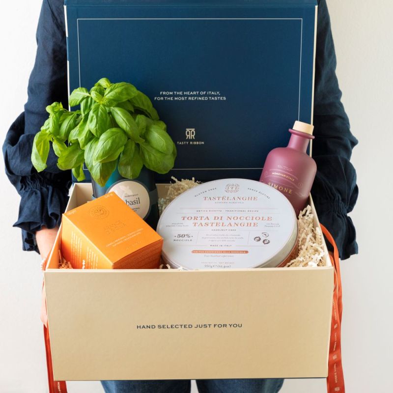 person holding open box of Italian treats including basil