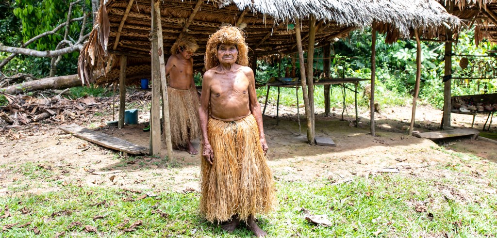 A Yaguan man wearing a distinctive long skirt made from Mauritia palm fiber, along with a matching headdress.