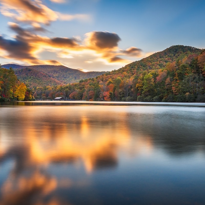 clouds over lake with fall foliage covered mountains in background atVogel State Park, Georgia