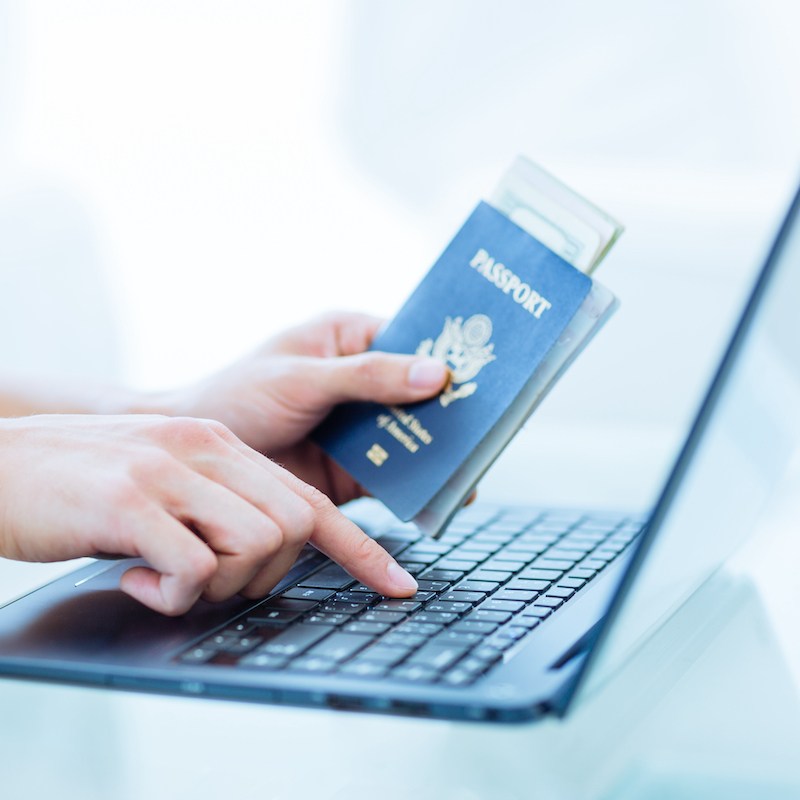 woman's hands, one holding passport, the other pressing key on laptop