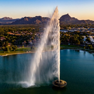 Aerial, drone, view of the Fountain Hills Park Fountain in Fountain Hills, Arizona with blue water, clear sky and landmark mountains