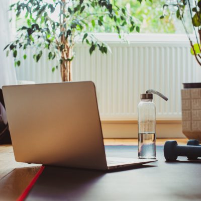 Laptop with fitness classes next to dumbbells and water bottle