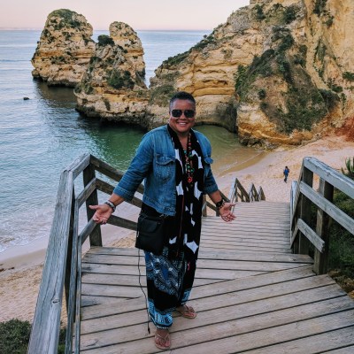 Irma C. standing on stairs leading to a beach near a rocking outcropping in the ocean.