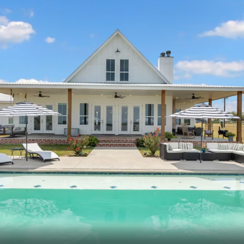 white farmhouse with a pool against the blue sky