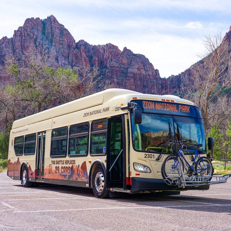 A new electric shuttle bus in front of The Watchman in Zion National Park