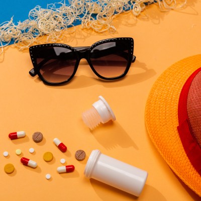 Colorful pills on orange background with sunglasses and hat. Concept of protection from allergy to the sun and sickness in the summertime on the pandemic situation.