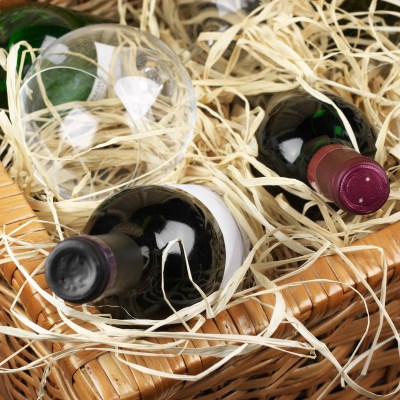 Picnic basket with bottles of red and white wine and wineglass in straw.