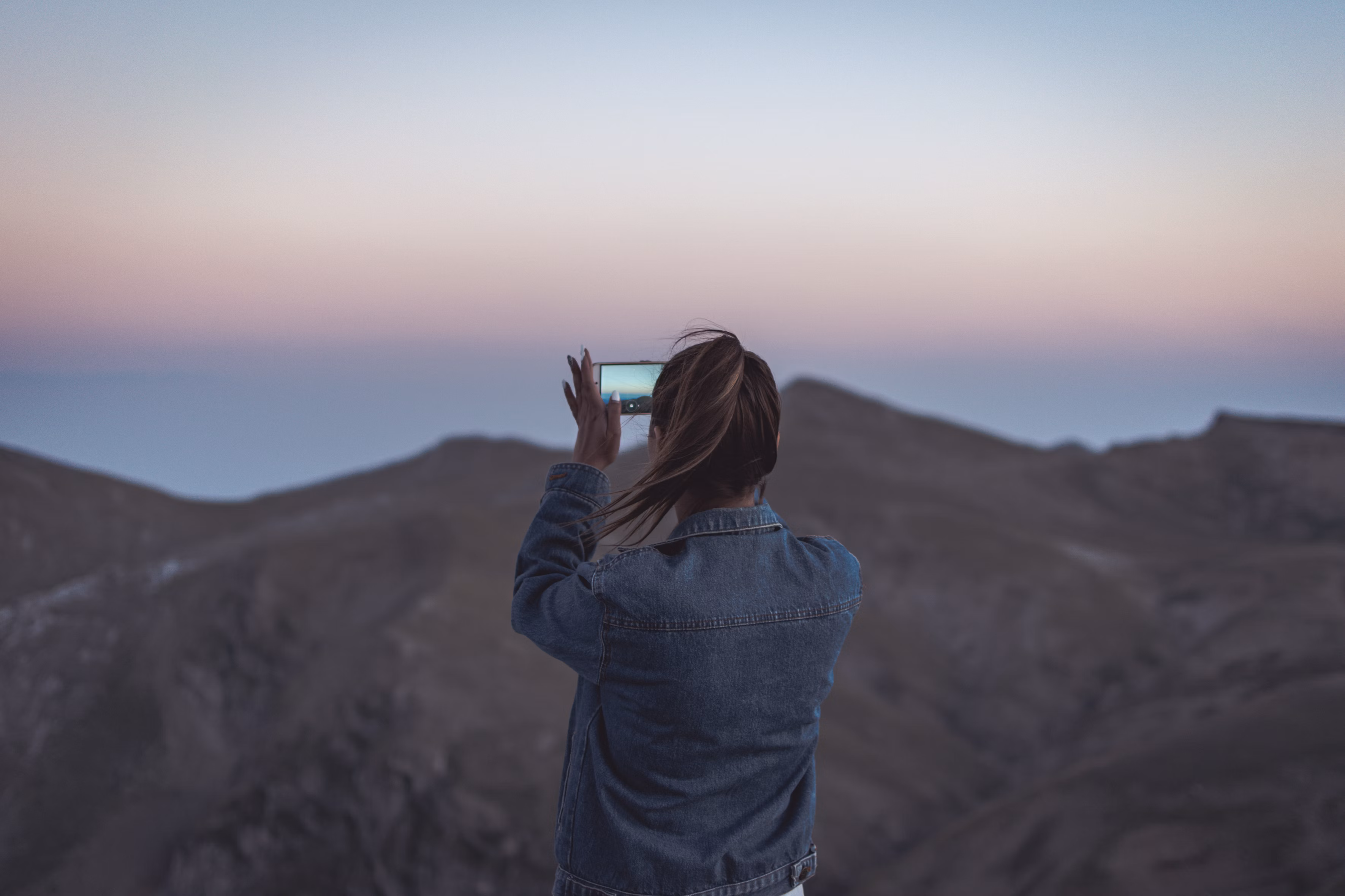 woman in blue denim jacket taking picture of mountain